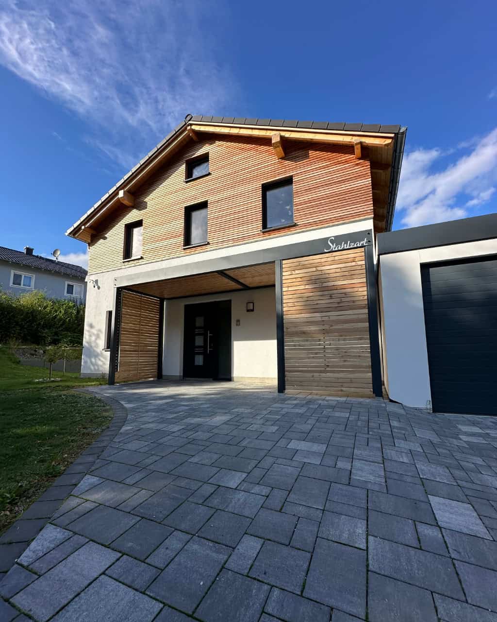 Modernes Stahlzart Vordach in Anthrazit mit Seitenteilen und Deckenverkleidung aus Holz, das den Eingangsbereich eines Hauses mit der angrenzenden Garage verbindet.