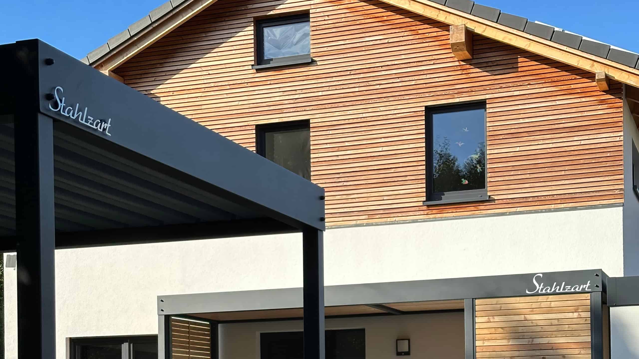 Eine Design-Kombination von Stahlzart: im Vordergrund ein moderner Stahl-Carport und dahinter das passende Vordach am Hauseingang, beide in Anthrazit mit Flachdach.