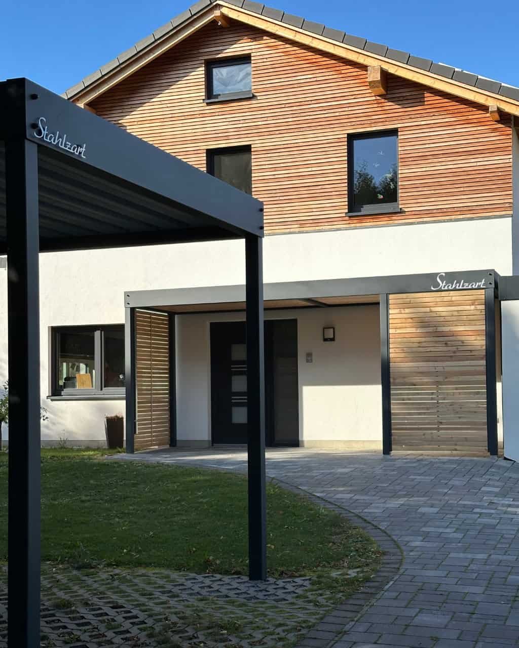 Eine Design-Kombination von Stahlzart: im Vordergrund ein moderner Stahl-Carport und dahinter das passende Vordach am Hauseingang, beide in Anthrazit mit Flachdach.